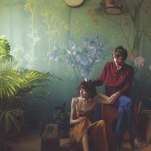 Para; młody mężczyzna i młoda kobieta na tle malarskiej, kwiecistej , fantazyjnej ściany; po lewej stronie żywe zielone rośliny